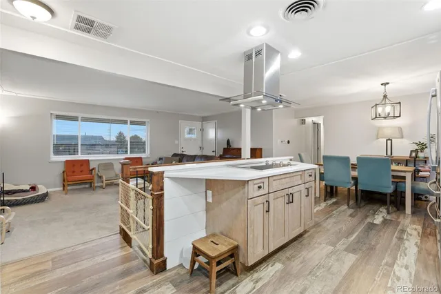 a open kitchen with stainless steel appliances kitchen island a stove a refrigerator a dining table and chairs with the wooden floor