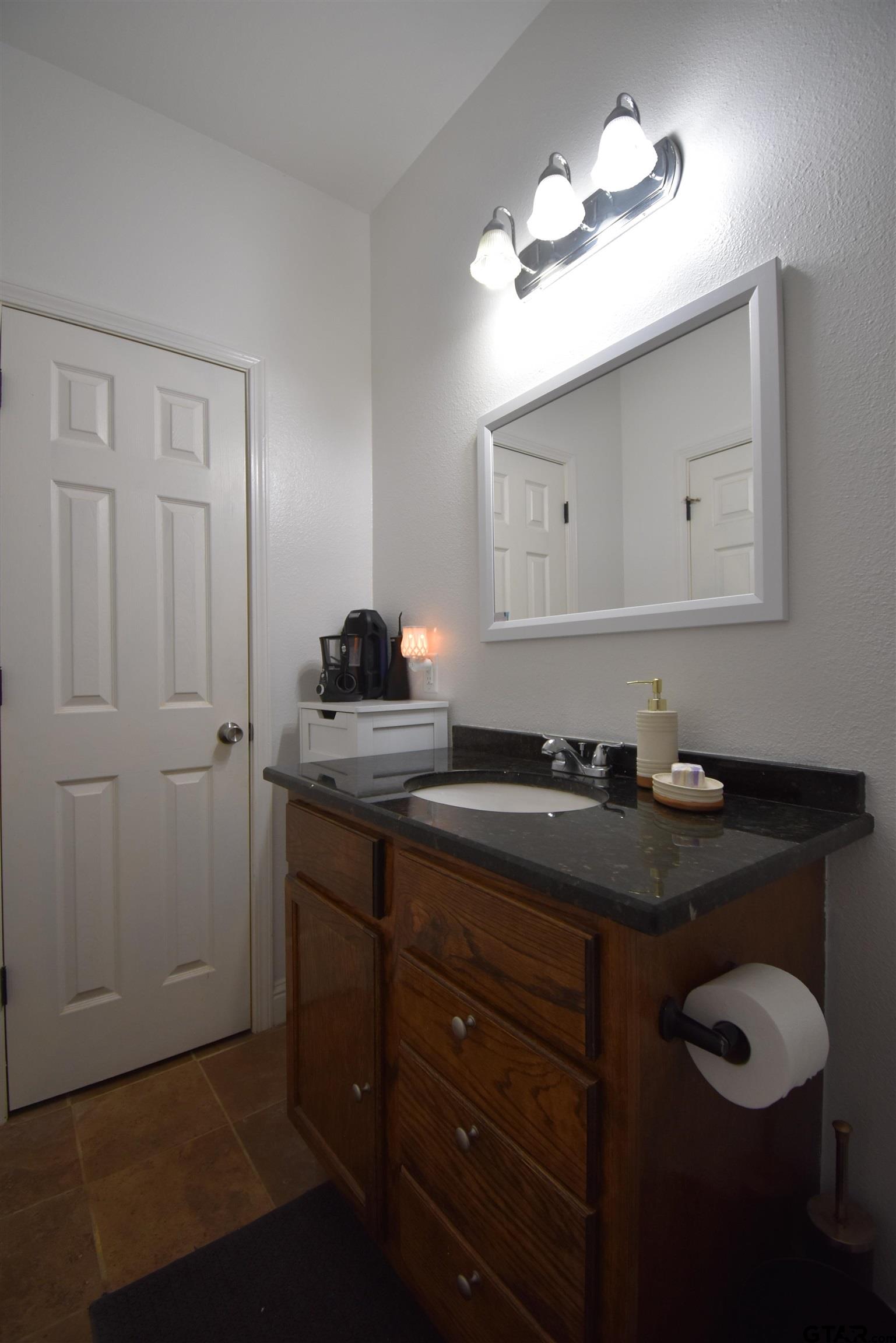 7727 Knowles Trace Tyler, TX 75708 - Photo 21 of 34 a bathroom with a granite countertop sink a light fixture and a mirror
