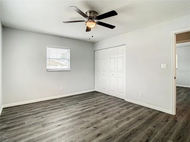 a view of an empty room with wooden floor and a ceiling fan