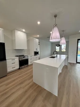 a large kitchen with stainless steel appliances a sink stove and wooden floor