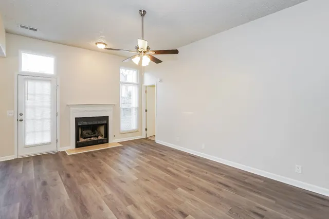a view of a livingroom with a fireplace a ceiling fan and wooden floor