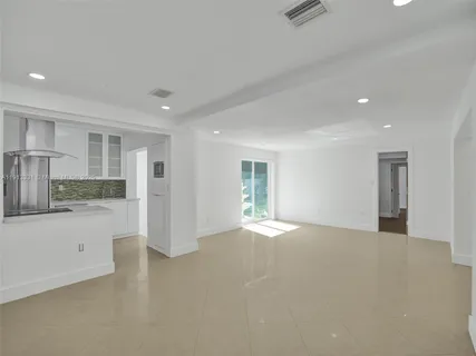 a view of an empty room with kitchen and window