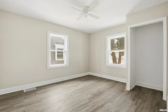 an empty room with wooden floor ceiling fan and windows