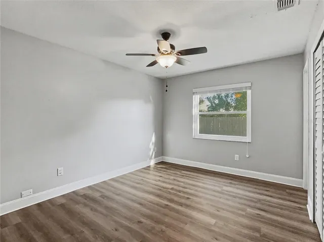 an empty room with wooden floor chandelier fan and windows