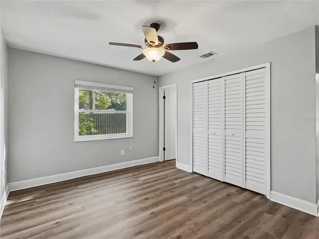 an empty room with wooden floor chandelier fan and windows