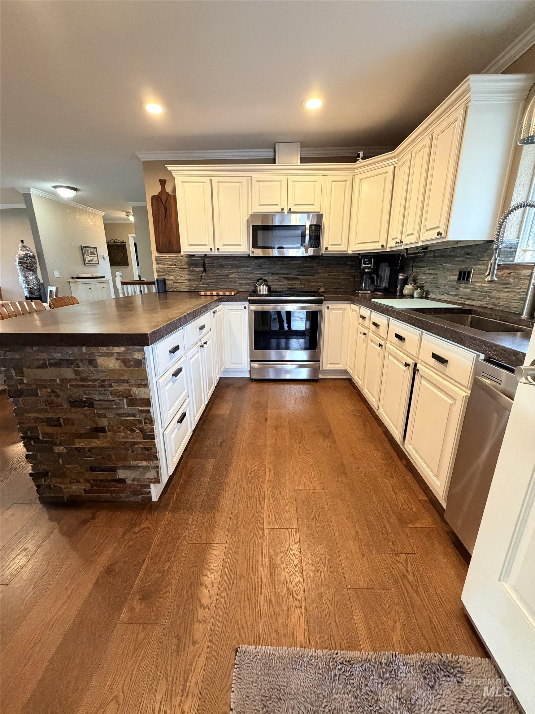 1306 Hemlock Avenue Lewiston, ID 83501 - Photo 8 of 38 Kitchen with stainless steel appliances, a peninsula, crown molding, dark wood finished floors, and decorative backsplash