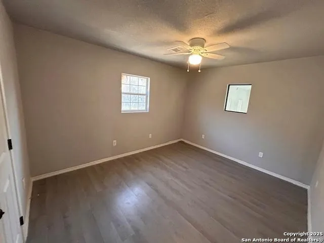 an empty room with wooden floor chandelier fan and windows
