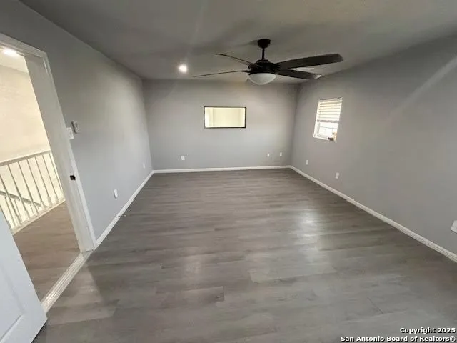 an empty room with wooden floor fan and windows
