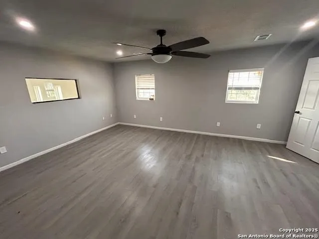 an empty room with wooden floor a ceiling fan and windows