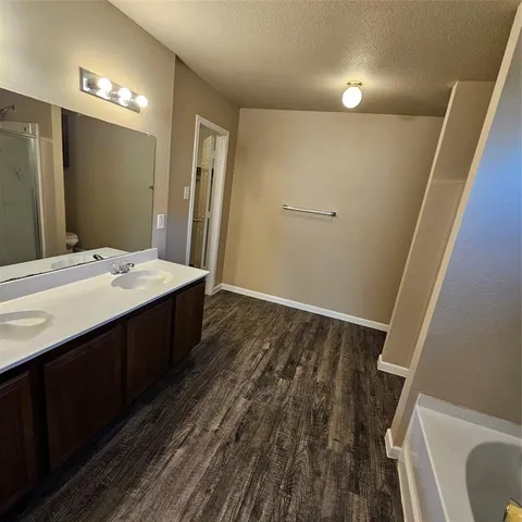 a view of a hallway with wooden floor and a bathroom