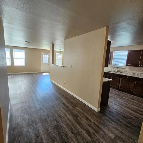 an empty room with wooden floor and a kitchen