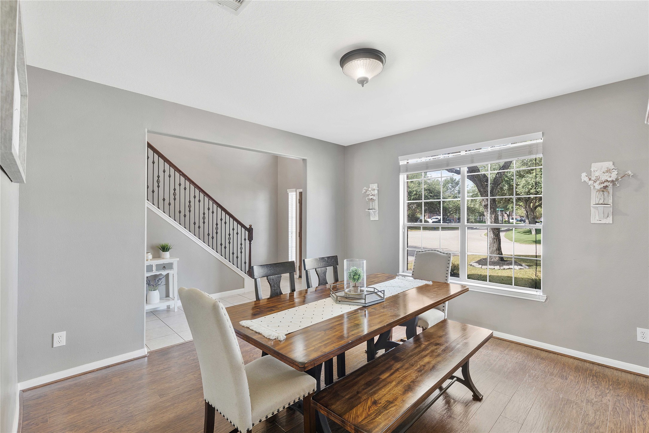 24506 Fort Path Drive Spring, TX 77373 - Photo 10 of 46 Bright dining area with a large window, offering abundant natural light and a view of the outdoors. The space features a stylish wooden table with matching chairs and a bench, complemented by elegant gray walls and wood plank flooring.