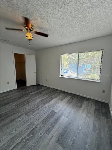 an empty room with wooden floor chandelier fan and windows