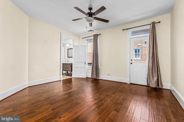 an empty room with wooden floor a ceiling fan and kitchen view