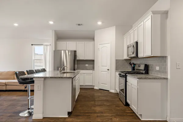 a kitchen with stainless steel appliances granite countertop a stove top oven a refrigerator a sink and dishwasher with wooden floor