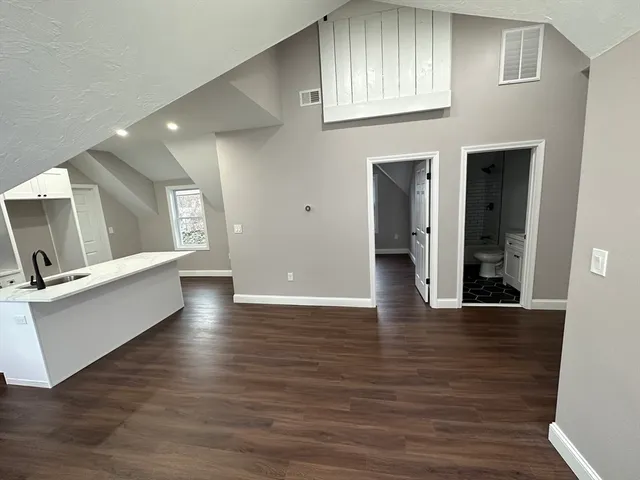 a view of an empty room with wooden floor and a kitchen