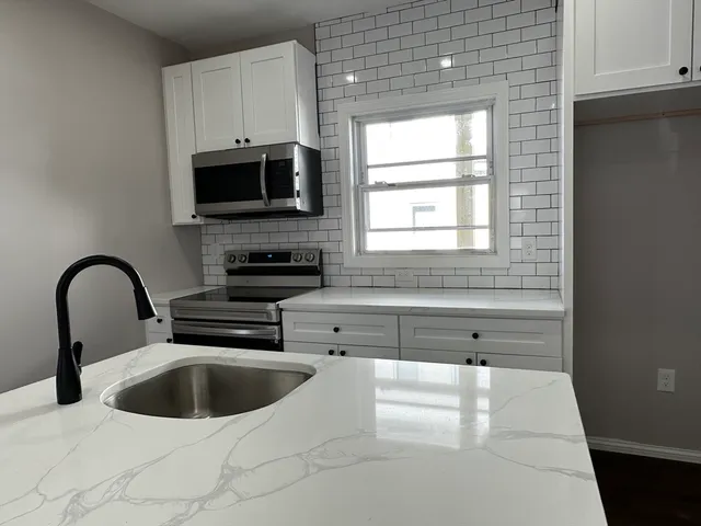 a kitchen with stainless steel appliances a sink a stove a microwave a window and white cabinets