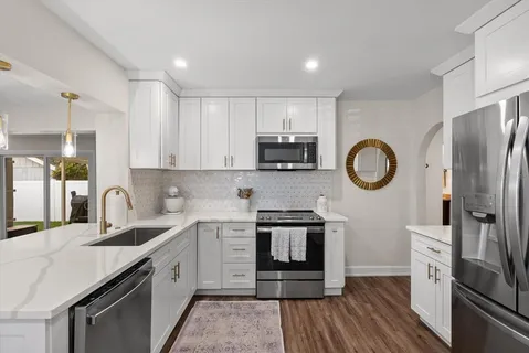 a kitchen with stainless steel appliances granite countertop a stove a sink dishwasher a refrigerator white cabinets and wooden floor