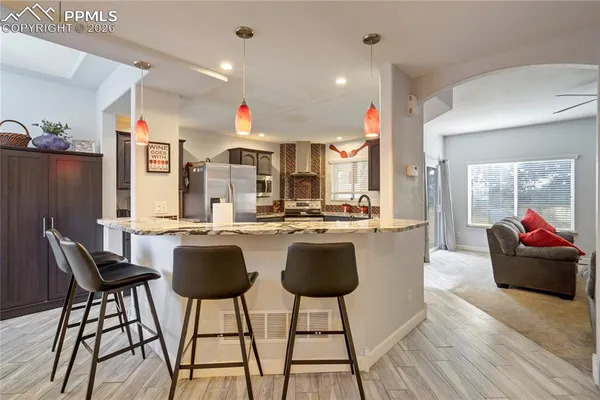a kitchen with stainless steel appliances kitchen island granite countertop a dining table chairs and a refrigerator