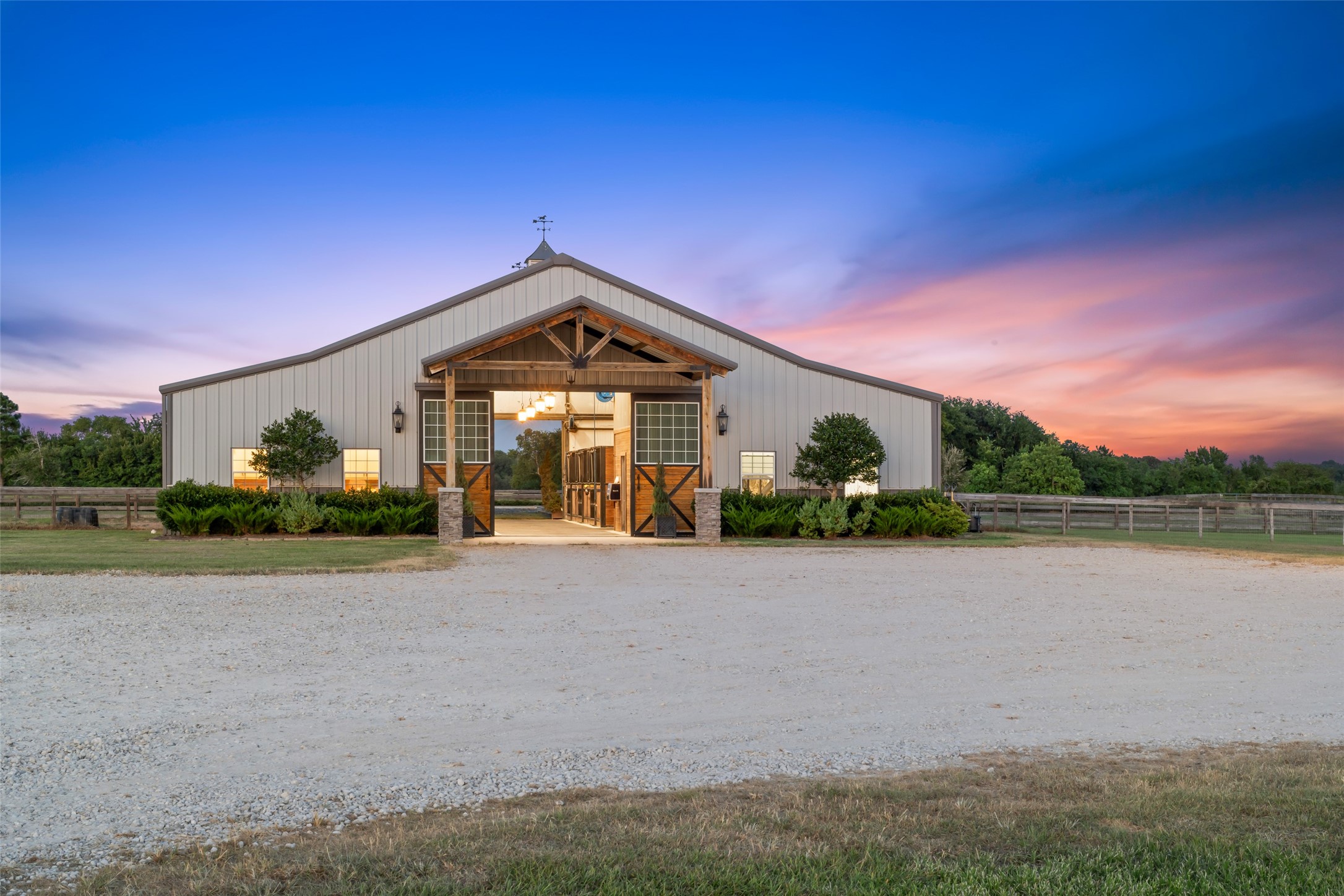 24118 Margerstadt Road Hockley, TX 77447 - Photo 3 of 50 At dusk, the barn glows with welcoming light, showcasing its symmetry, craftsmanship, and breezeway aisle stretching through the center.