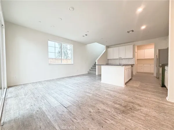 a view of kitchen and an empty room with wooden floor