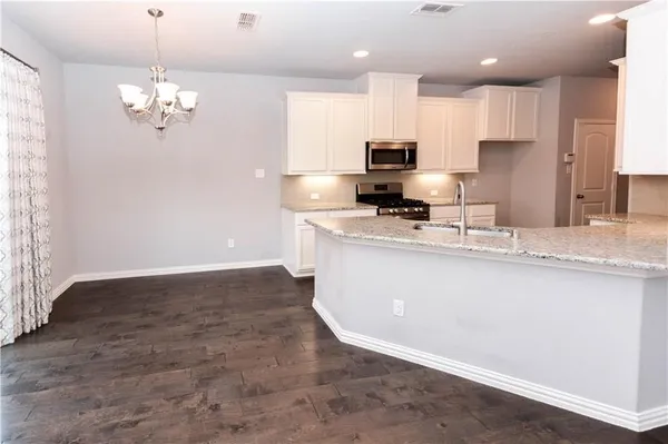 a kitchen with kitchen island granite countertop stainless steel appliances a sink a stove a refrigerator cabinets and a chandelier