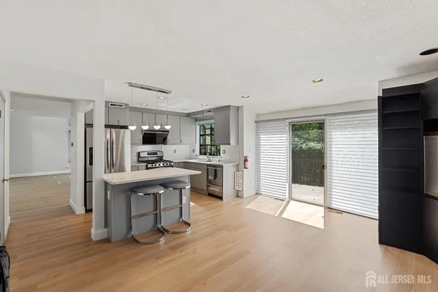 a kitchen with stainless steel appliances kitchen island granite countertop a stove a refrigerator a sink a dining table and chairs with wooden floor