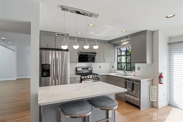 a kitchen with stainless steel appliances kitchen island granite countertop a stove a refrigerator a sink dishwasher a dining table and chairs with wooden floor