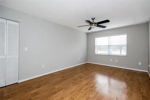 an empty room with wooden floor ceiling fan and windows
