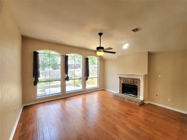 a view of an empty room with wooden floor fireplace and a window