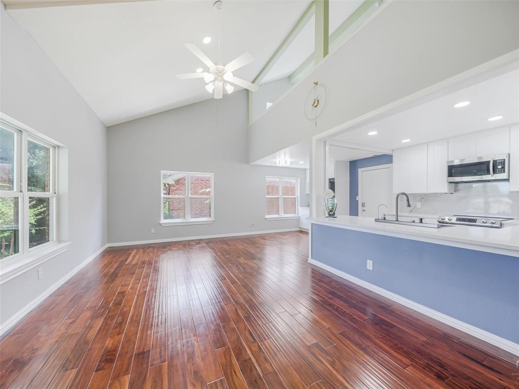 1716 East Parker Road Plano, TX 75074 - Photo 7 of 25 Vaulted ceiling with a ceiling fan and recessed lighting, wood-finish flooring, white trim throughout, and a kitchen pass-through with a light blue accent wall