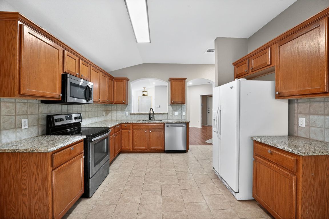 1502 McDowell Bend Leander, TX 78641 - Photo 17 of 31 a kitchen with stainless steel appliances granite countertop a stove a sink dishwasher a refrigerator and a microwave