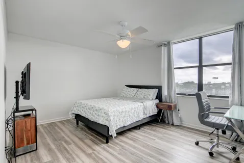 a bedroom with a bed a large window with table and chair