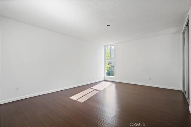 an empty room with wooden floor and windows with curtains