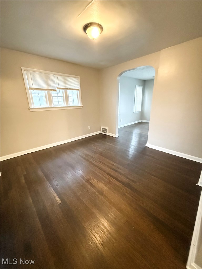 Spare room featuring arched walkways, healthy amount of natural light, and dark wood-style floors