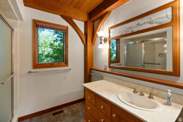 435 Canyon Road Millville, UT 84326 - Photo 20 of 113 Bathroom featuring exposed timber beams, a wood-framed window, and a vanity with a light-toned countertop and wood cabinetry