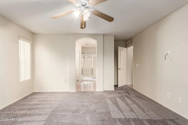 an empty room with chandelier fan and windows