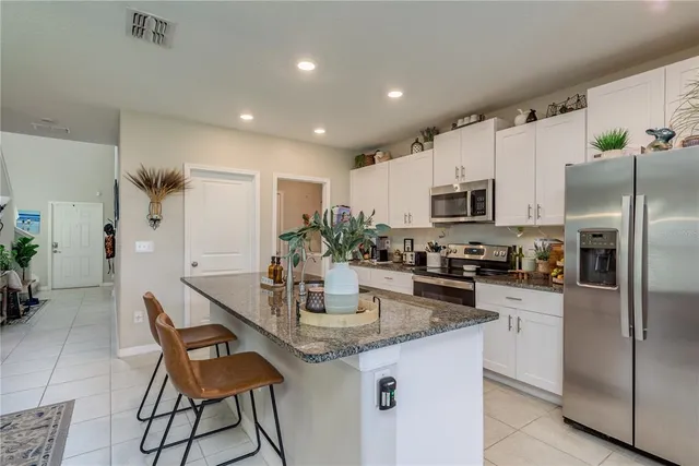 a kitchen with kitchen island granite countertop a table chairs microwave and refrigerator