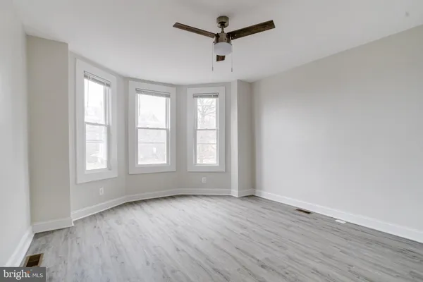 an empty room with wooden floor ceiling fan and windows