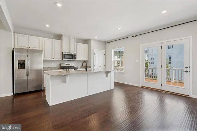 a kitchen with stainless steel appliances granite countertop a refrigerator a stove a sink and white cabinets with wooden floor next to windows