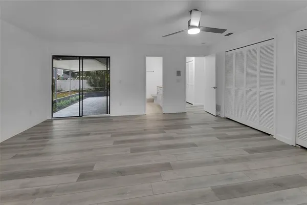 a view of an empty room with wooden floor and a ceiling fan