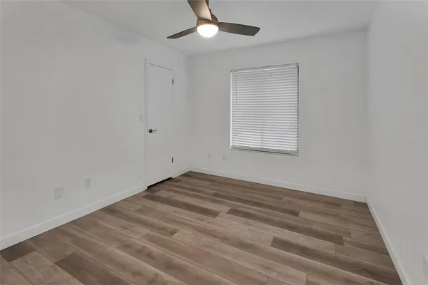 an empty room with wooden floor chandelier fan and windows