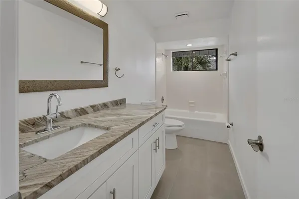 a bathroom with a granite countertop sink a toilet a mirror and shower