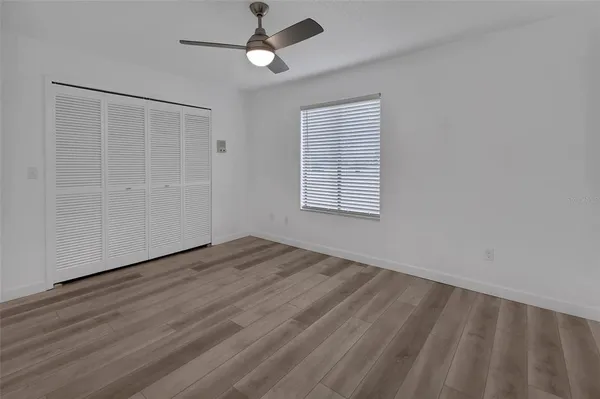 an empty room with wooden floor chandelier fan and windows