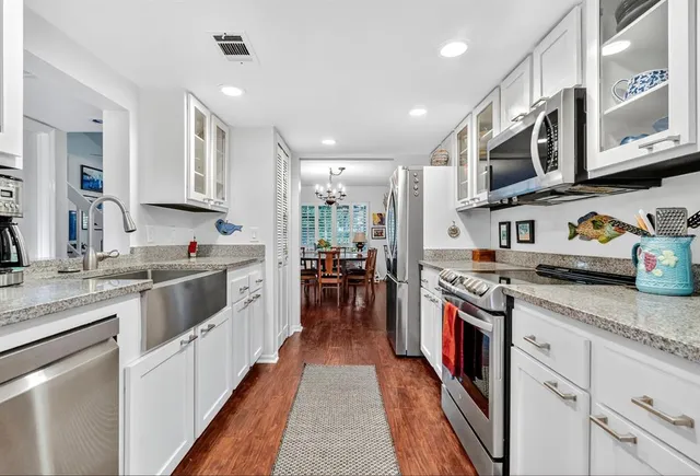 a kitchen with stainless steel appliances granite countertop a stove top oven a sink dishwasher and white cabinets with wooden floor