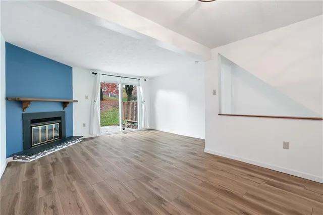a view of an empty room with wooden floor fireplace and a window