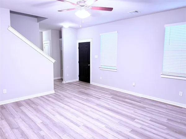 a view of an empty room with wooden floor and a ceiling fan
