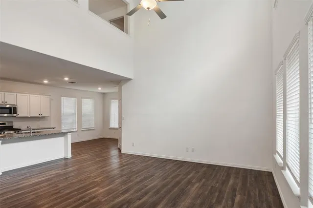 an empty room with wooden floor kitchen view and windows