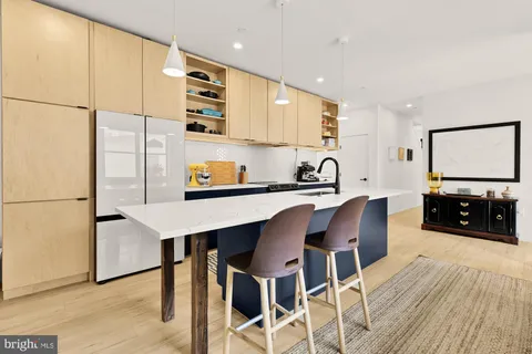 a kitchen with stainless steel appliances a sink a stove a refrigerator a dining table and chairs with wooden floor