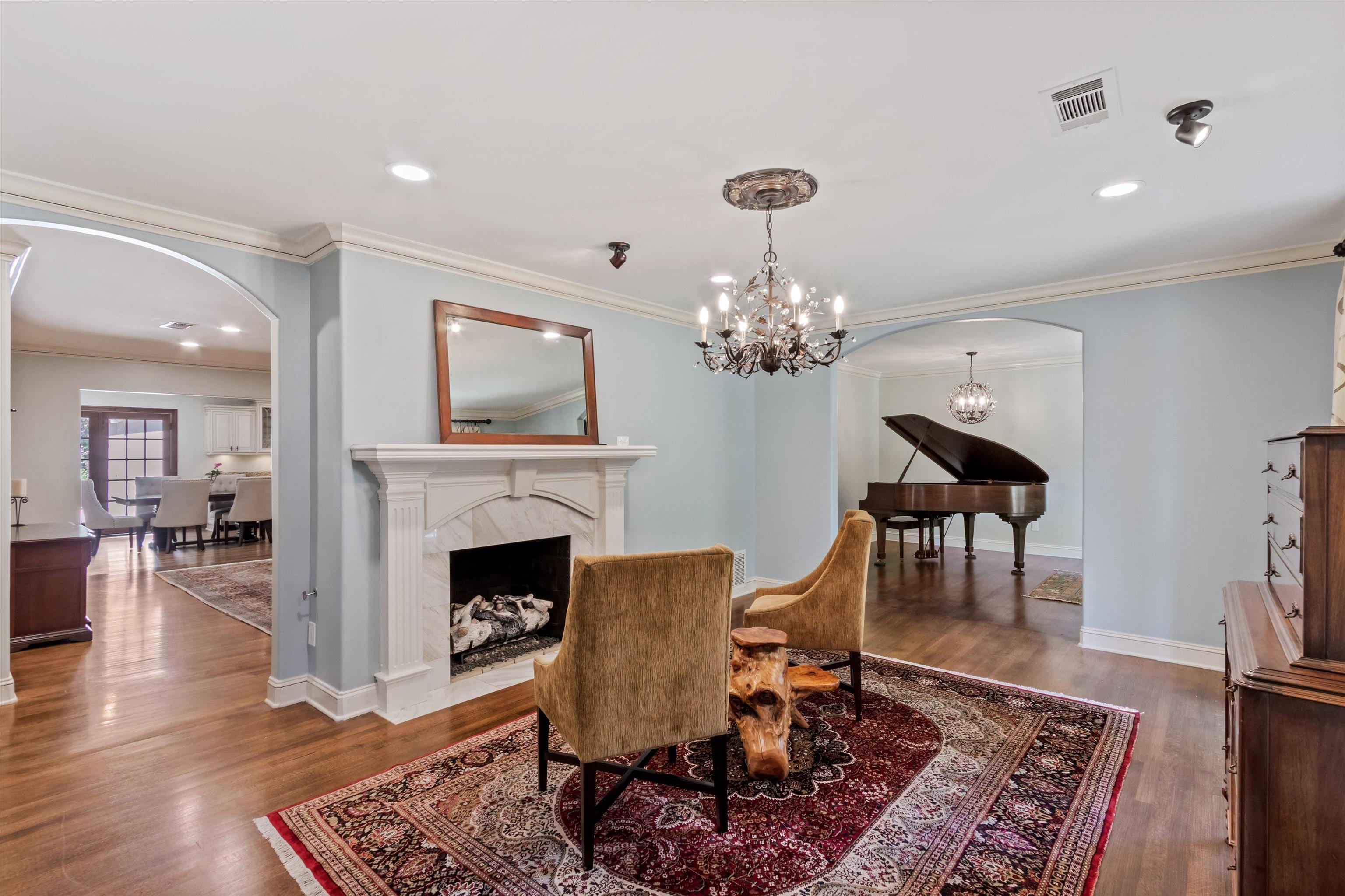 5302 South Angela Road Memphis, TN 38120 - Photo 8 of 40 Living area featuring a white mantel fireplace with a marble-style surround, wood-finish flooring, an arched entryway, crown molding, and a chandelier with a ceiling medallion